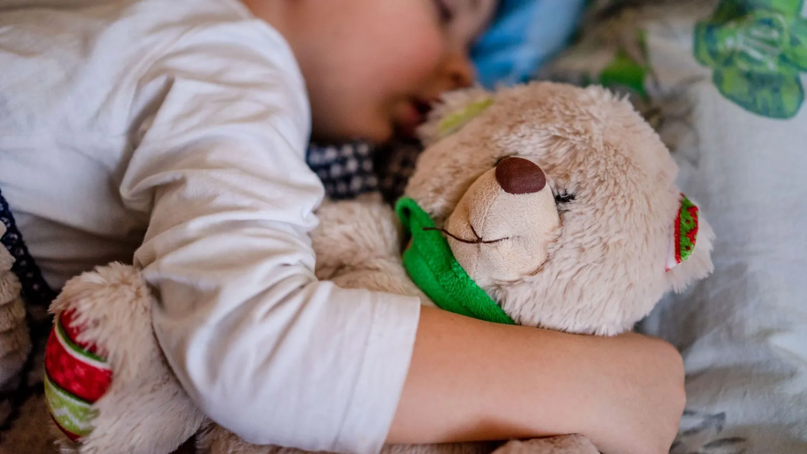 Kind schläft ruhig in seinem Bett und hält einen Teddybären im Arm