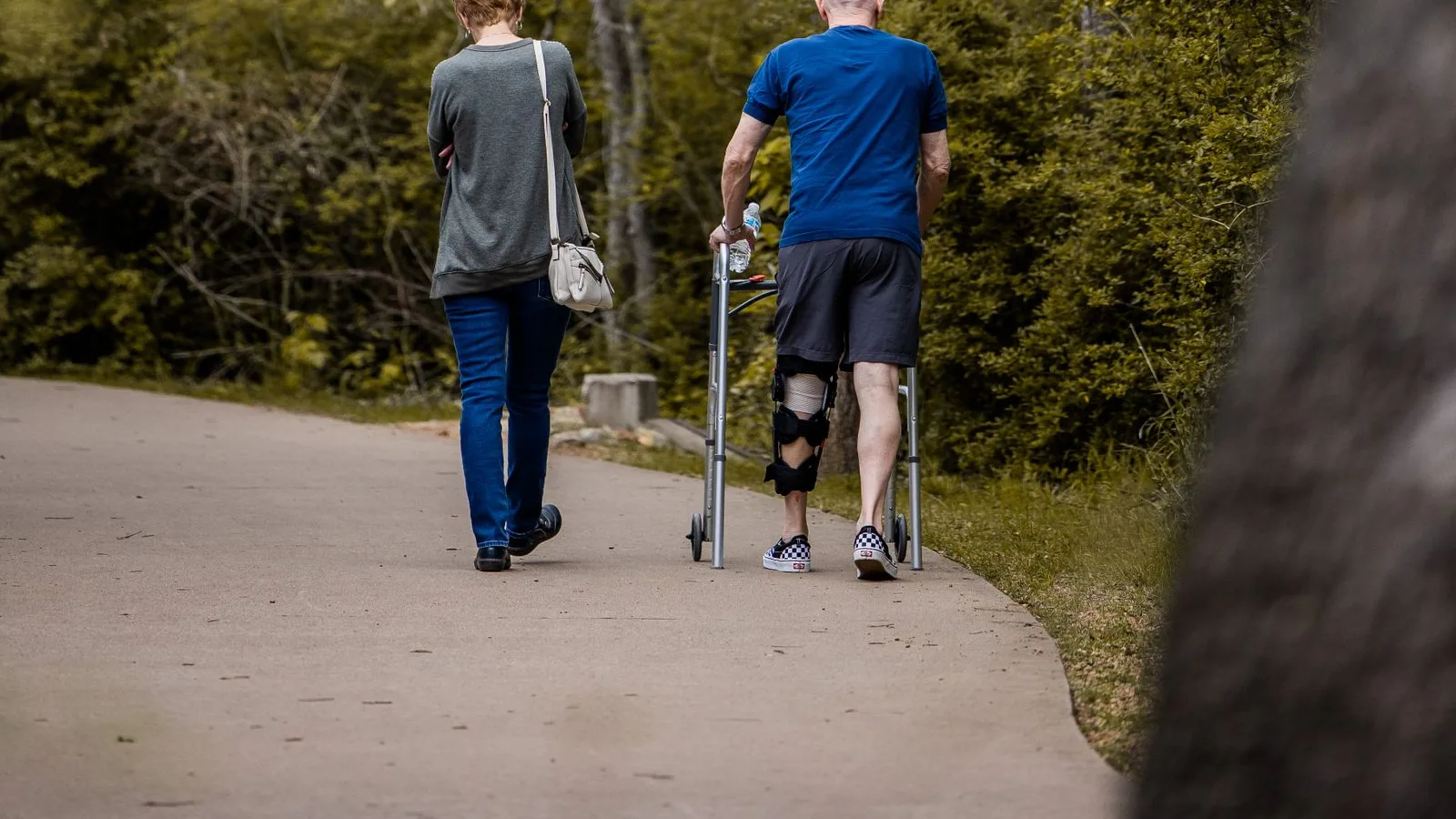 Mann mit Beinorthese geht mit einer Begleiterin auf einem Parkweg