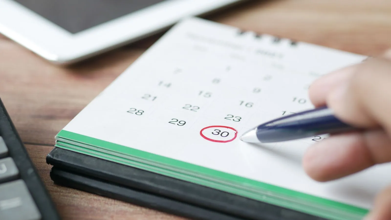 Hand mit Kugelschreiber an einem Tischkalender, ein Datum ist rot eingekreist