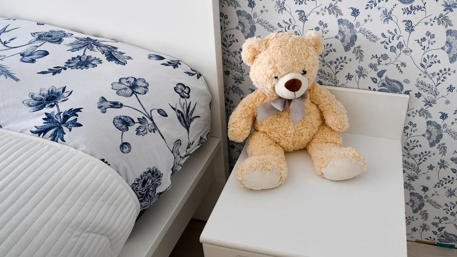 Kinderzimmer mit gemachtem Bett und einem Teddybären auf dem Nachttisch