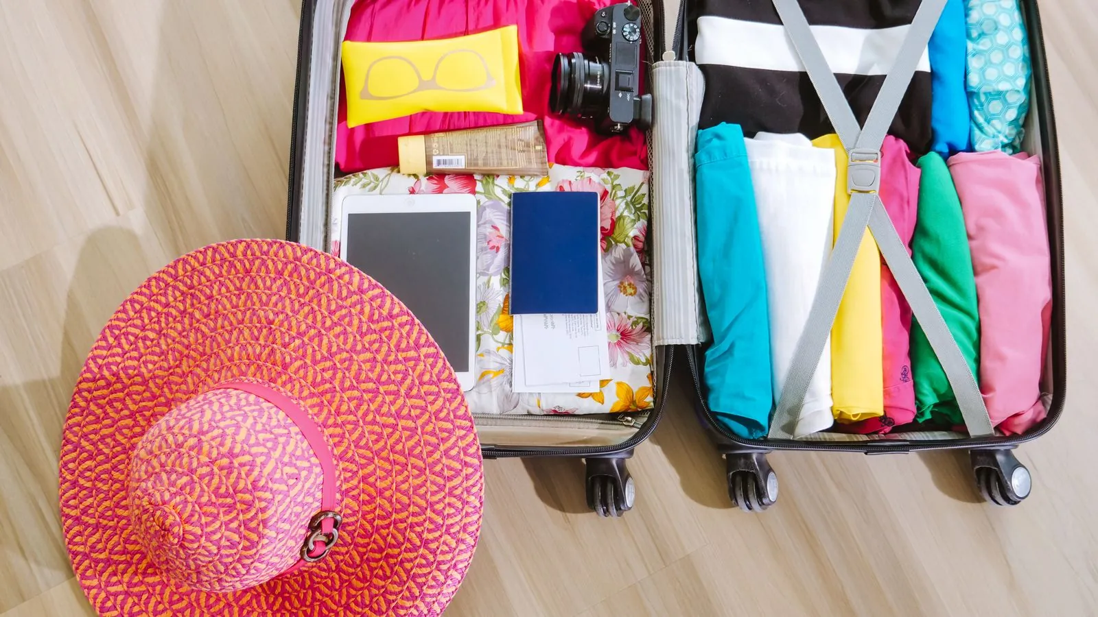 Gepackter Koffer von oben mit gerollter Kleidung, Sonnenhut, Kamera und Reisepass