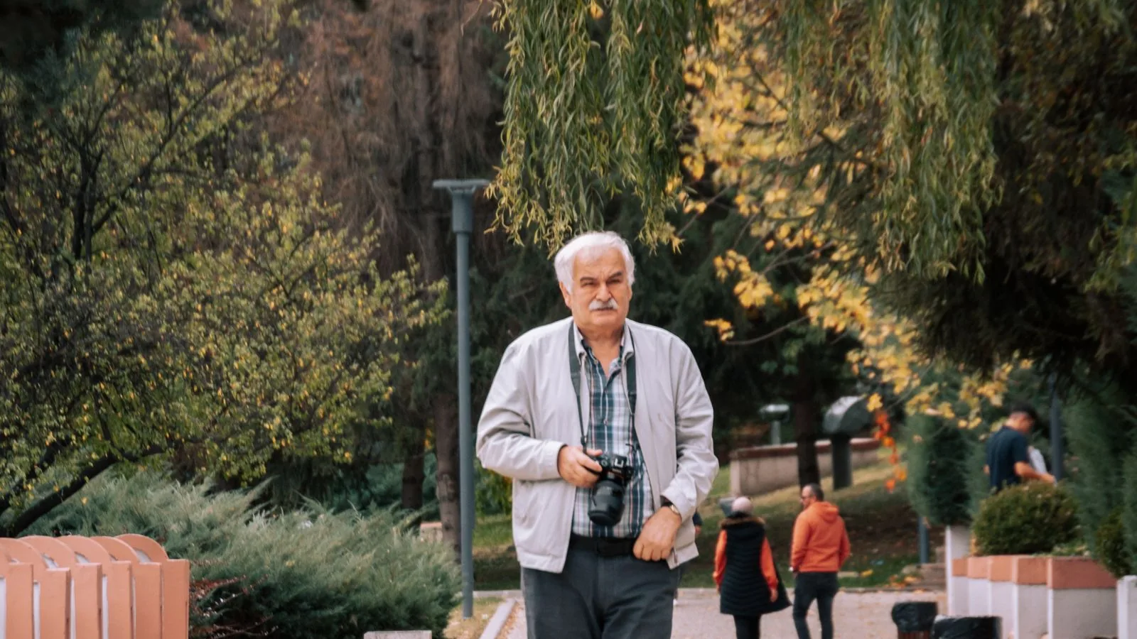 Älterer Mann geht mit einer Kamera in der Hand durch einen Park