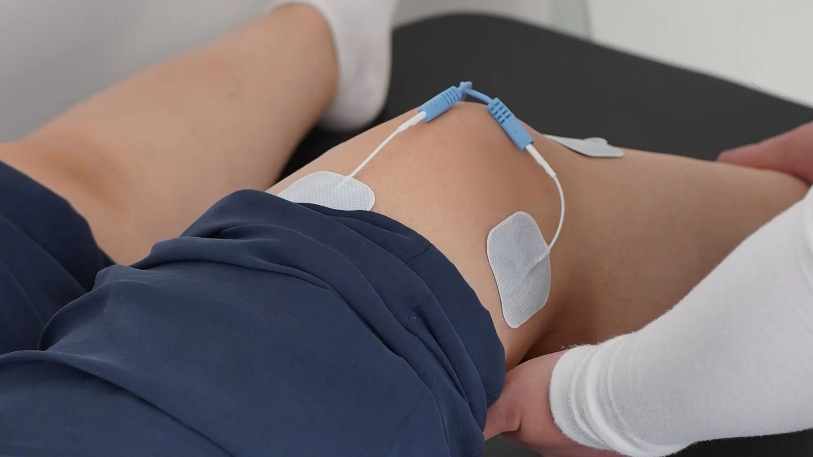 Zwei Klebeelektroden eines TENS-Geräts werden am Knie angebracht