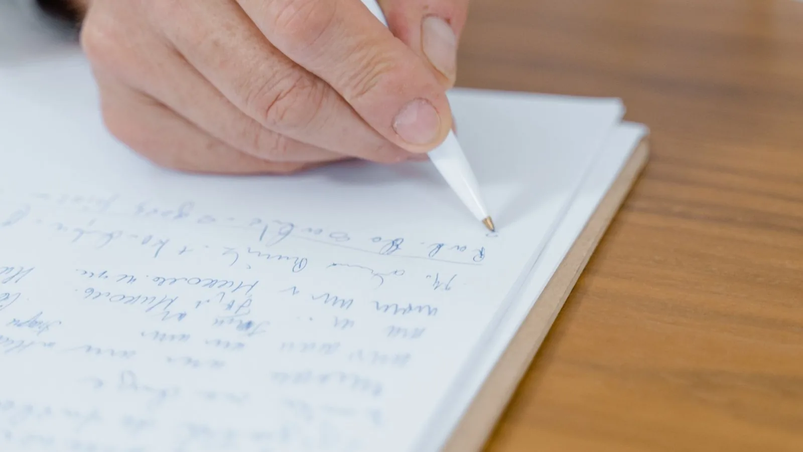 Hand mit Stift schreibt auf einen Notizblock auf einem Holztisch